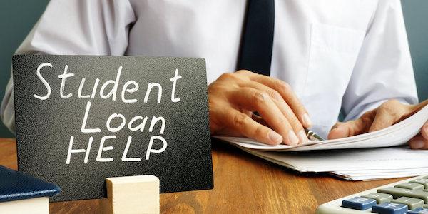 A sign reading "Student Loan Help" in front of a person looking at paperwork.